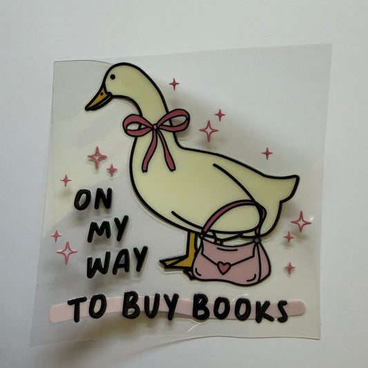 Sticker with a duck holding books and text 'On my way to buy books' on a white background