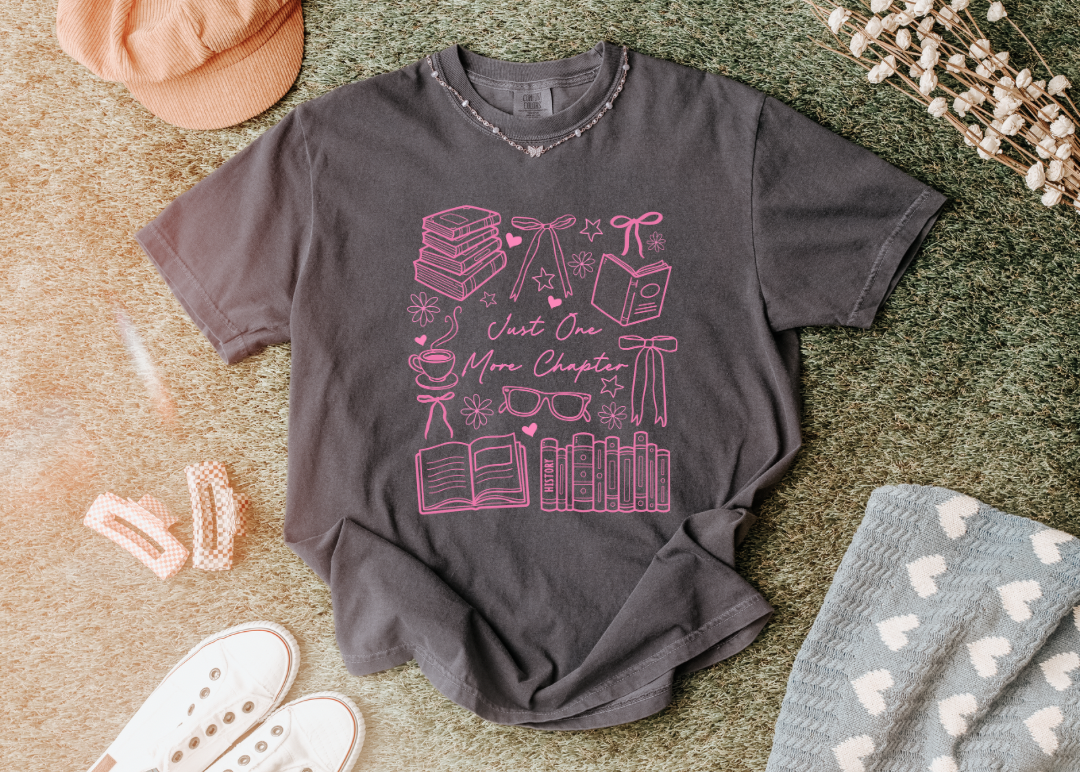 Gray t-shirt with pink graphic design on a textured surface with accessories.