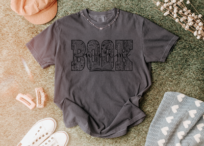 Gray t-shirt with text on a textured surface with accessories around