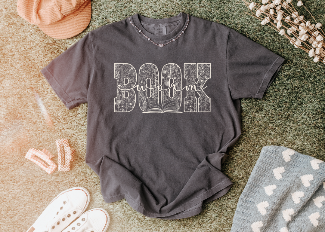 Gray t-shirt with 'Book worm' text on a textured surface with accessories.