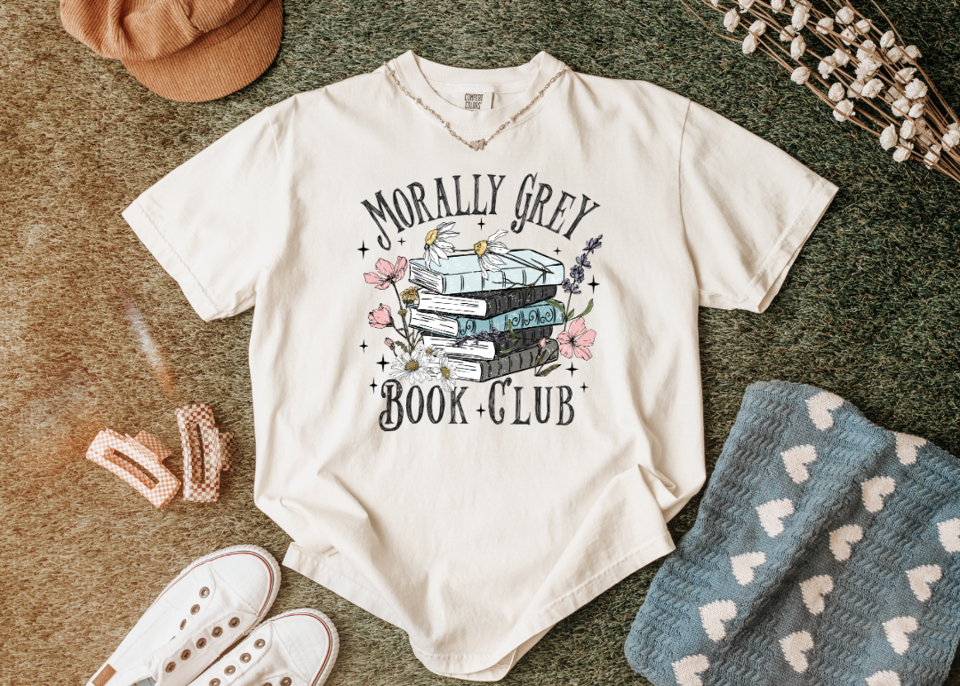 White t-shirt with 'Morally Grey Book Club' design on a textured surface with accessories.