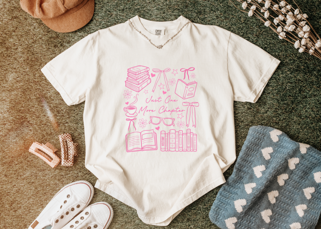 White t-shirt with pink graphic design on a textured surface with accessories.
