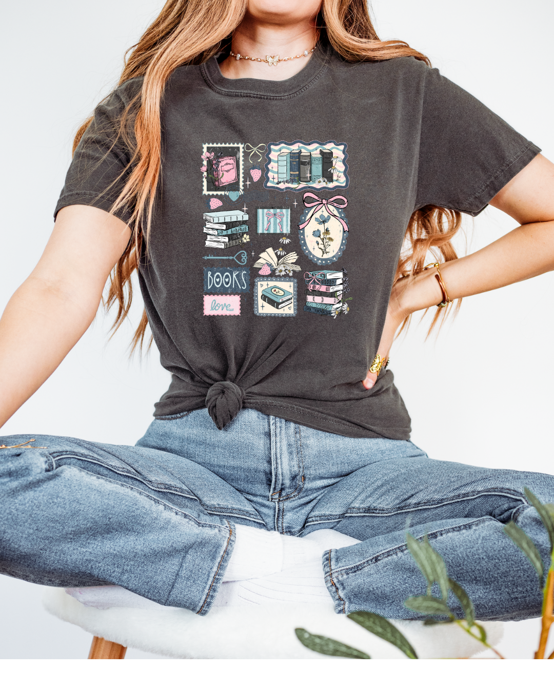 Person wearing a dark gray t-shirt with graphic designs and blue jeans, sitting on a white surface.