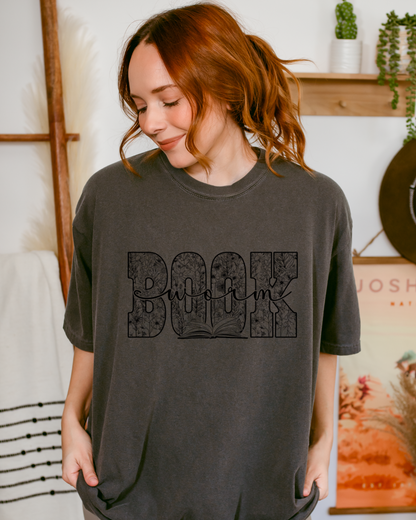 Woman wearing a dark gray t-shirt with 'Bookworm' printed on it in a casual setting.