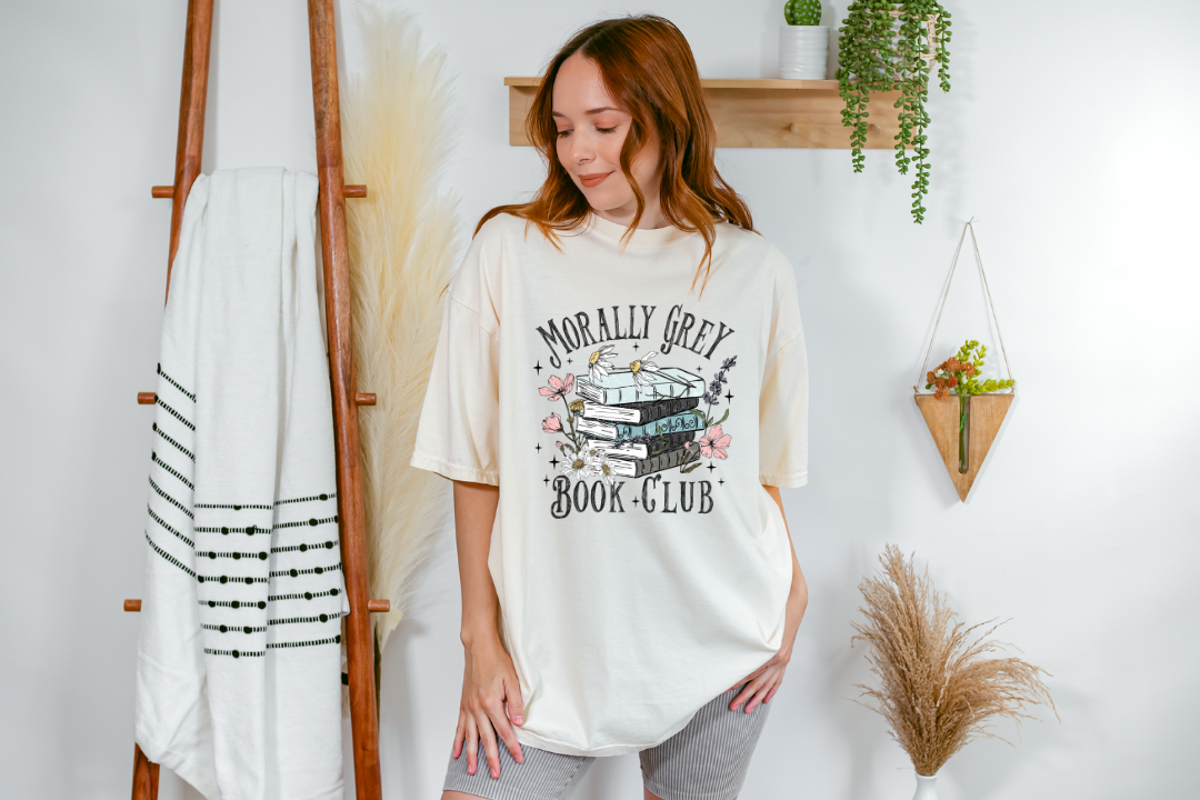 Woman wearing a 'Morally Grey Book Club' t-shirt in a room with decor elements.