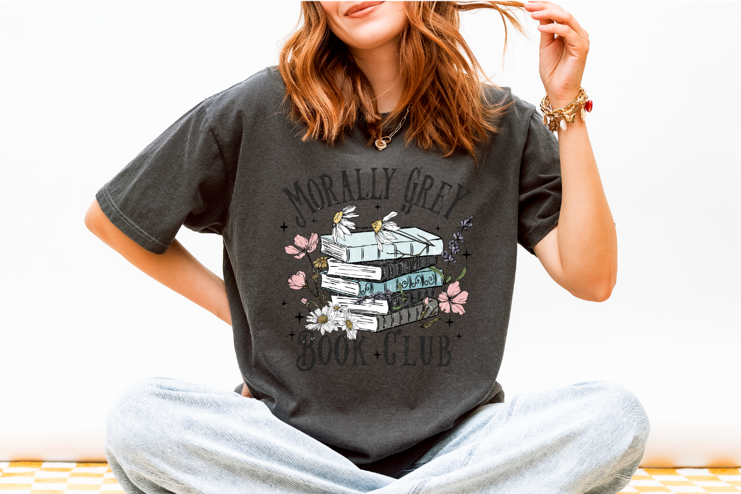 Person wearing a dark gray t-shirt with a graphic design and text, sitting on a white surface.
