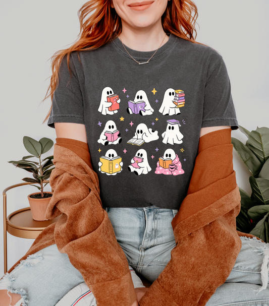 A woman wearing a dark gray graphic t-shirt with a cartoon ghost pattern, styled with a brown cardigan and light blue jeans in a cozy indoor setting.
