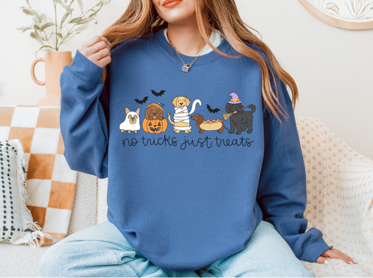 A woman wearing a blue crewneck sweatshirt with a graphic of four dogs dressed as Halloween characters and the text 'no tricks just treats', sitting on a patterned couch.